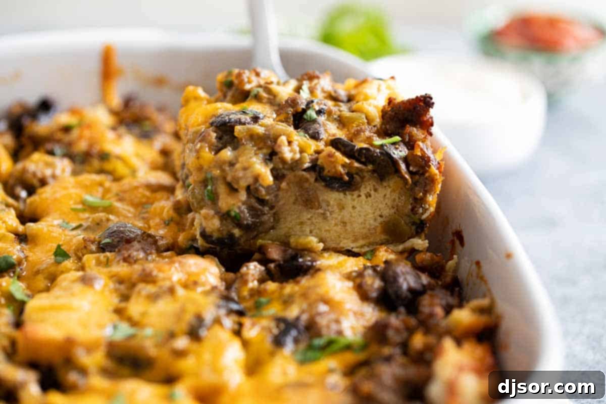 A serving spoon lifting a slice of Sausage Breakfast Casserole from the baking dish.