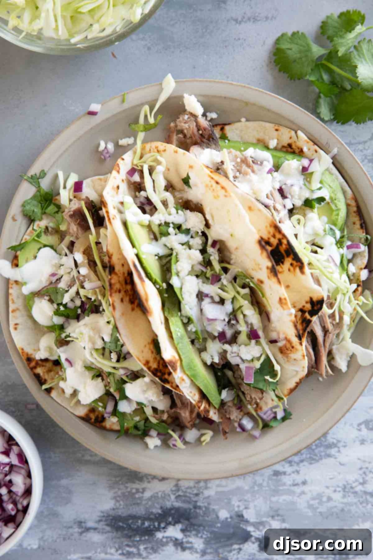 Three shredded pork tacos with charred tortillas on a plate.