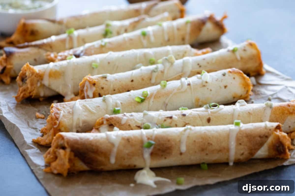Crispy Buffalo Chicken Taquitos drizzled with creamy blue cheese dressing and fresh herbs, arranged beautifully on parchment paper, perfect for a party appetizer.
