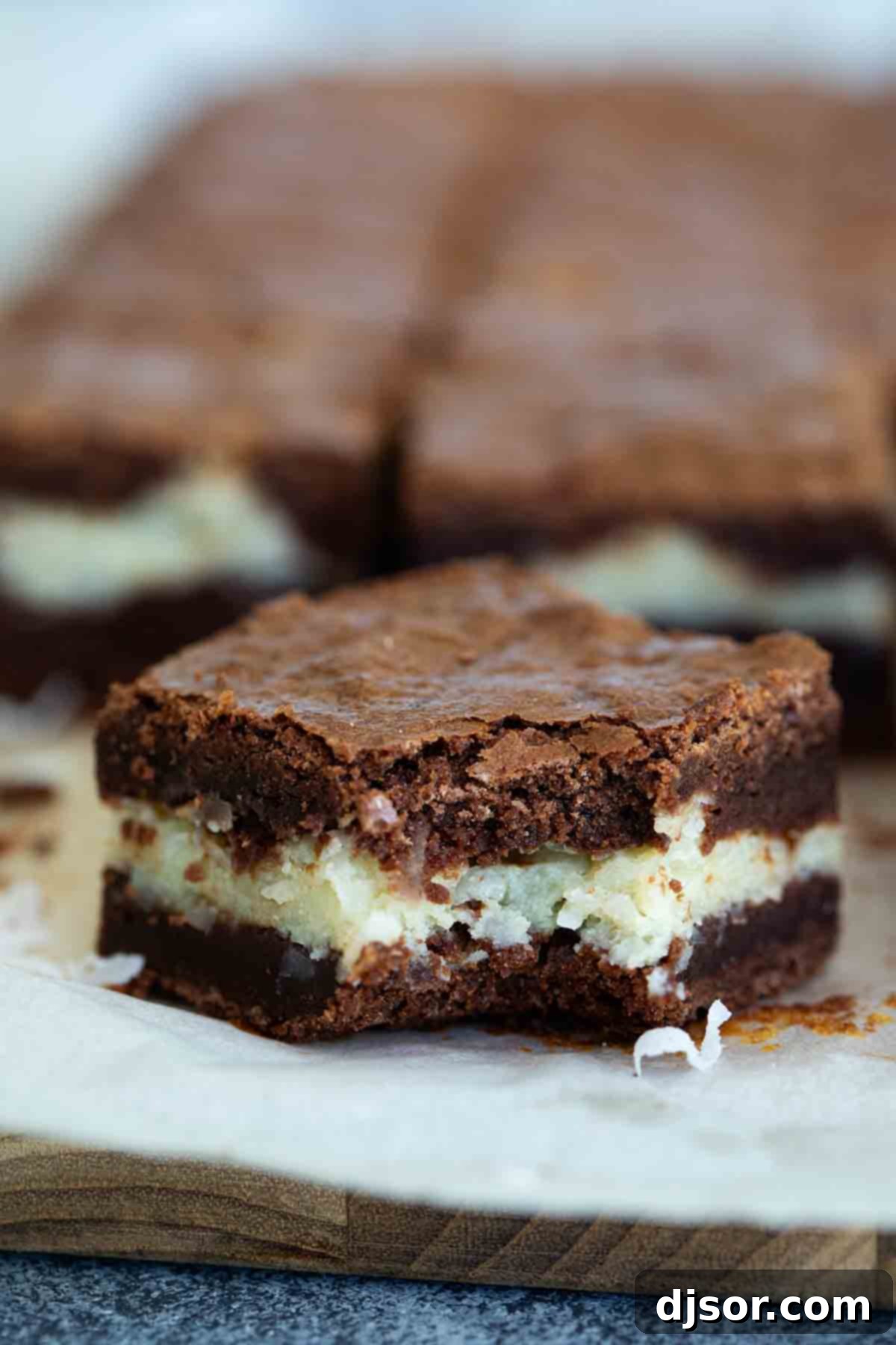 Close-up of a coconut brownie with a bite taken out, showcasing the fudgy chocolate texture and the distinct, creamy coconut layer.