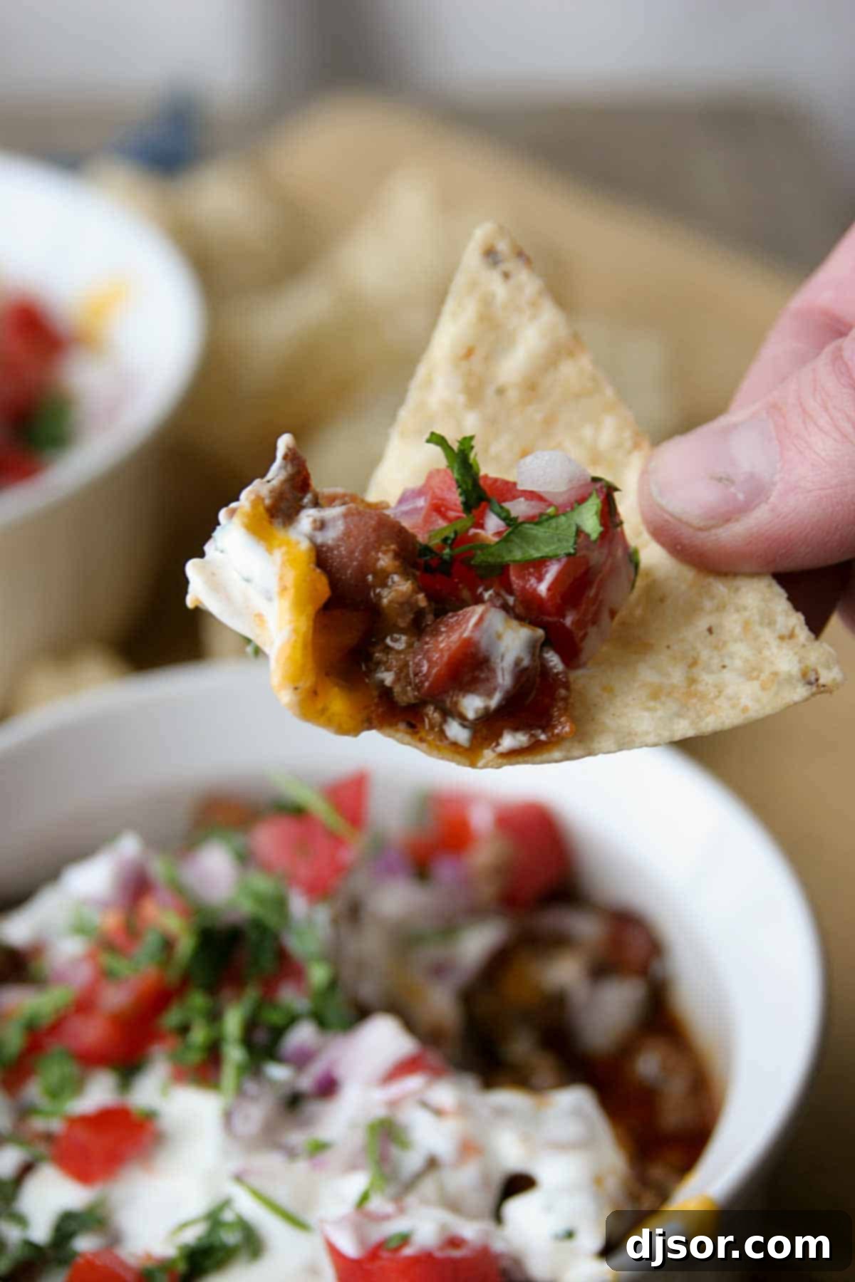 Scooping 7 Layer Chili Dog Dip with a tortilla chip