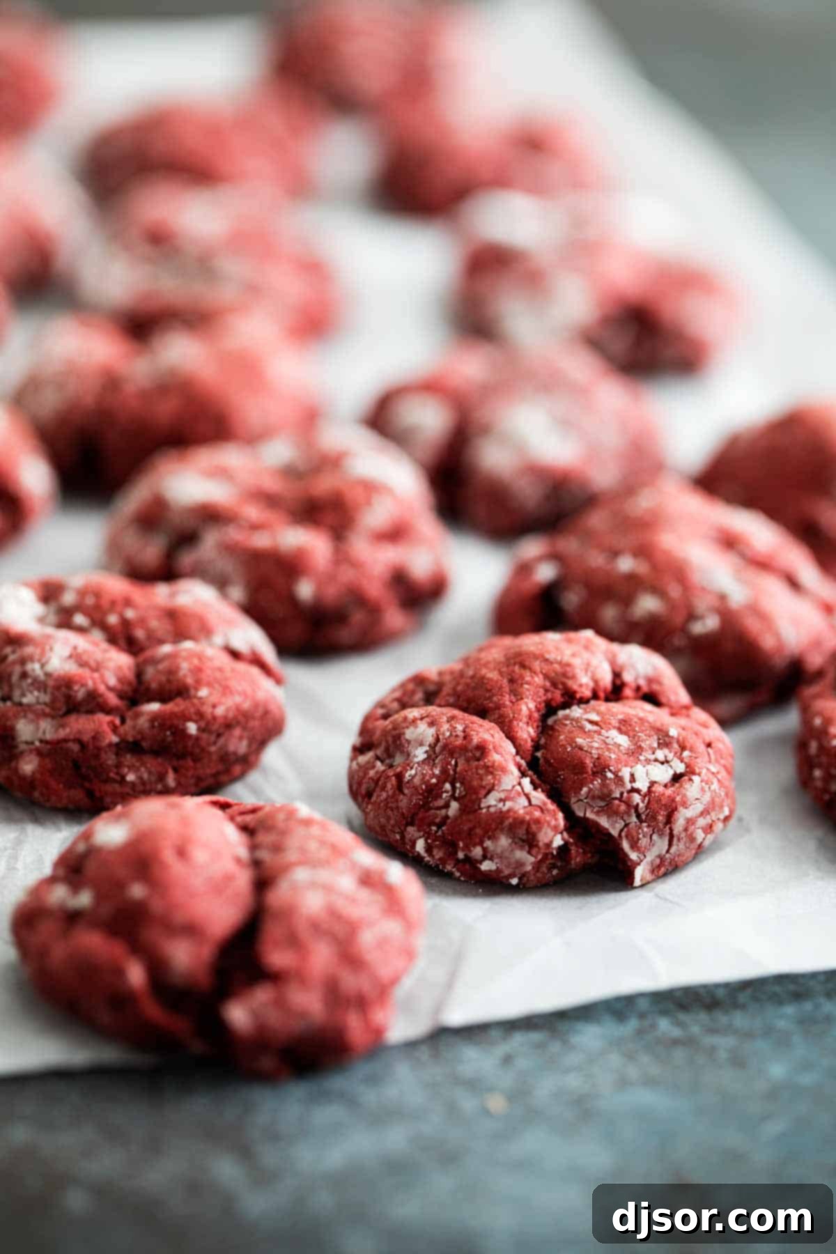 Red Velvet Gooey Butter Cookies on parchment paper, showcasing their soft, powdered sugar coating and irresistible texture.