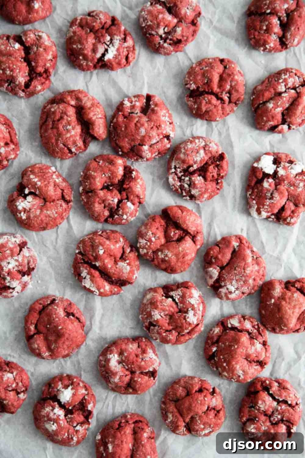 Close-up of red velvet gooey butter cookies with a generous coating of powdered sugar, stacked neatly on a white surface.