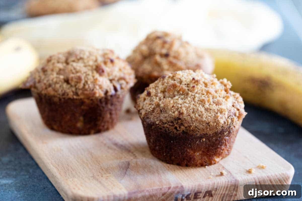 Delicious Banana Muffins with a Sweet Crumb Topping Three banana muffins with crumb topping on a cutting board, highlighting their golden-brown tops and moist interior.