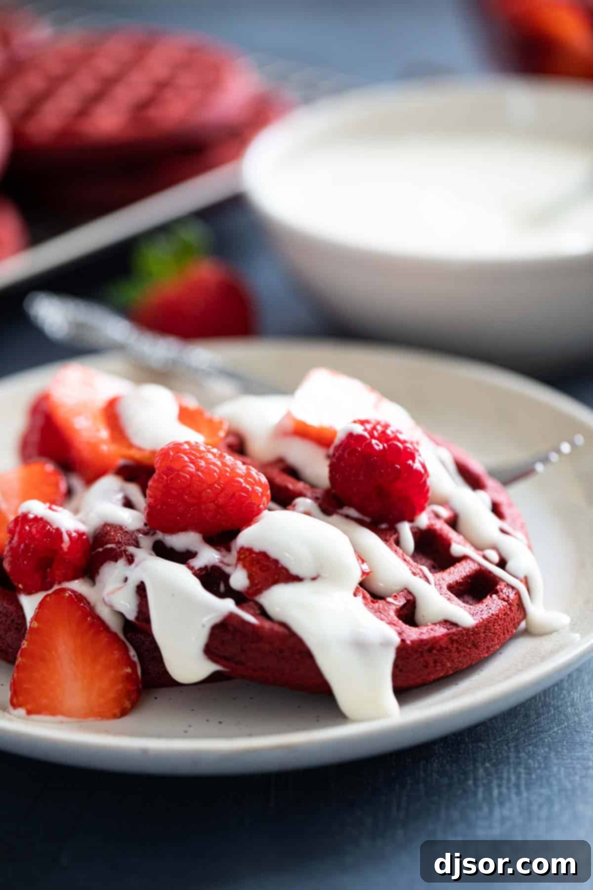 Fluffy red velvet waffles generously topped with a rich cream cheese drizzle, sliced fresh strawberries, and whole juicy raspberries.