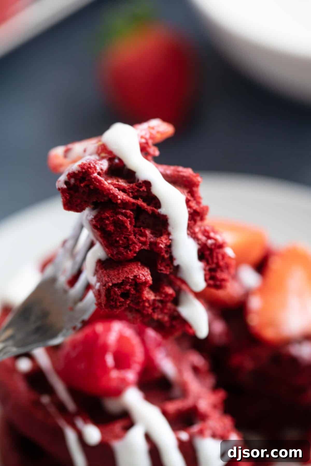 A close-up shot of a fork cutting into a red velvet waffle, revealing its soft interior and the rich toppings.