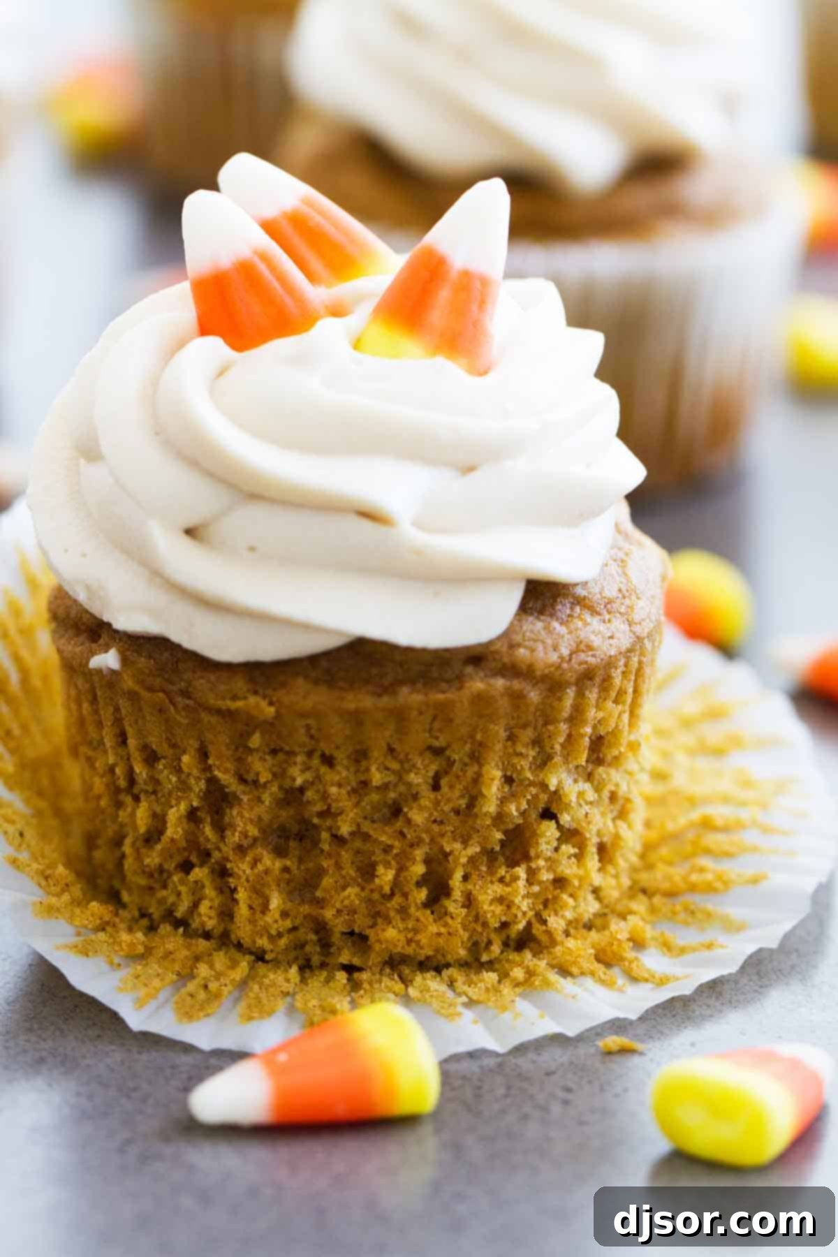 Effortless Autumn Pumpkin Treats 3 Close-up of a pumpkin cupcake generously frosted with brown sugar cream cheese frosting and topped with candy corn for a festive touch.