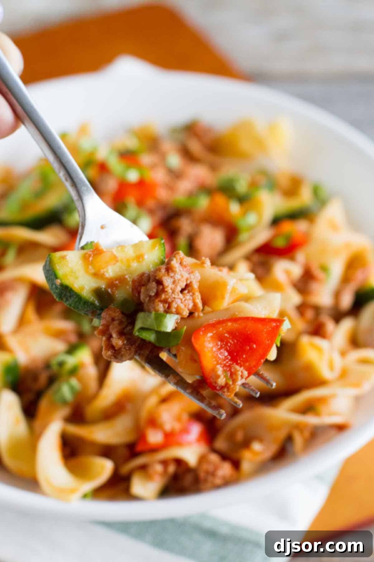 A fork holding a generous portion of Turkey Goulash, showing the mix of egg noodles, ground turkey, and colorful vegetables, perfectly coated in a rich tomato sauce.