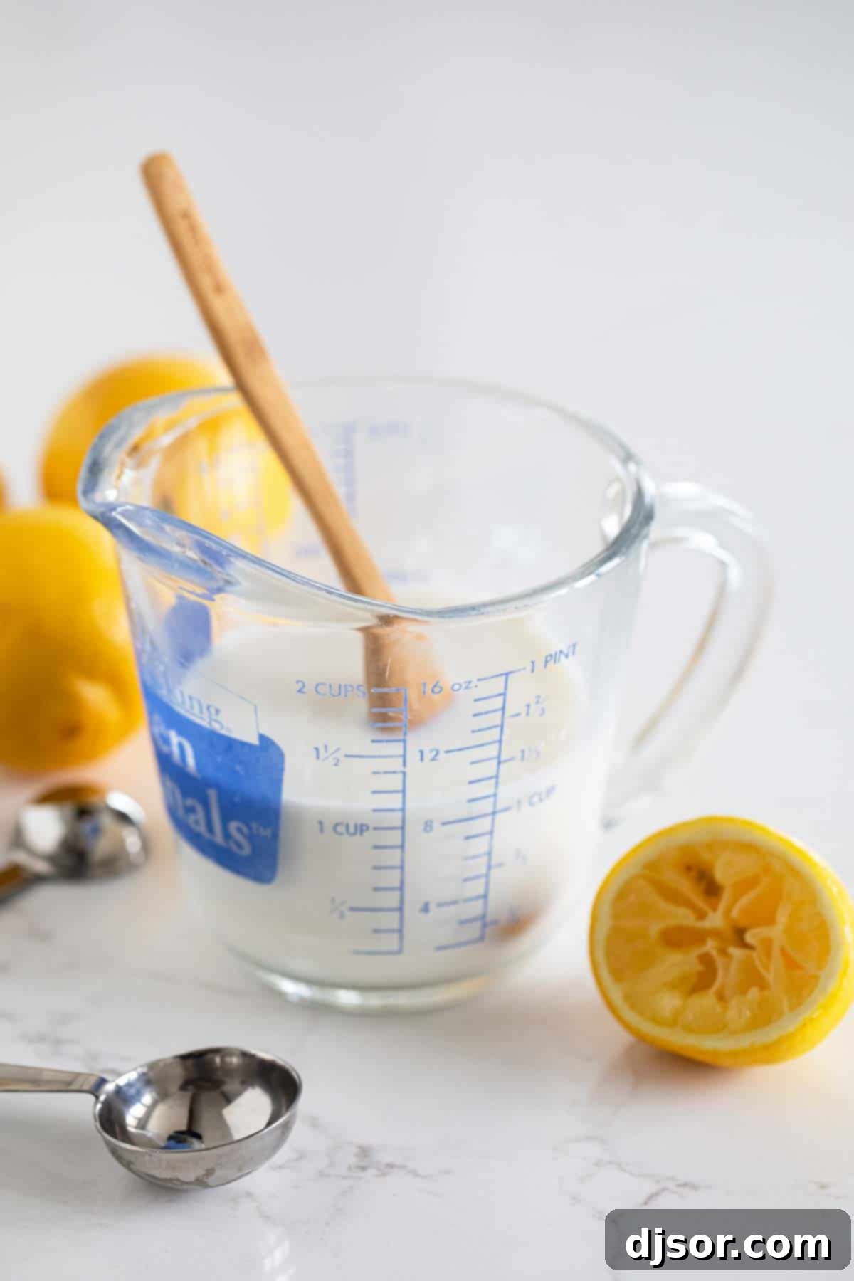 A glass of homemade buttermilk substitute with a lemon and a whisk, ready to be used