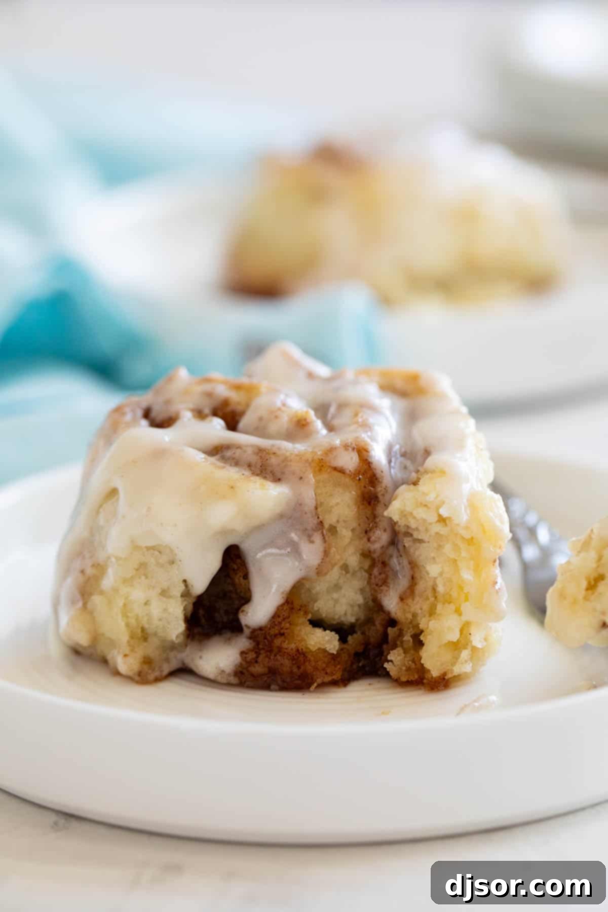 A close-up of a cinnamon biscuit on a plate with a bite taken out, revealing its soft, swirled interior and tempting icing.