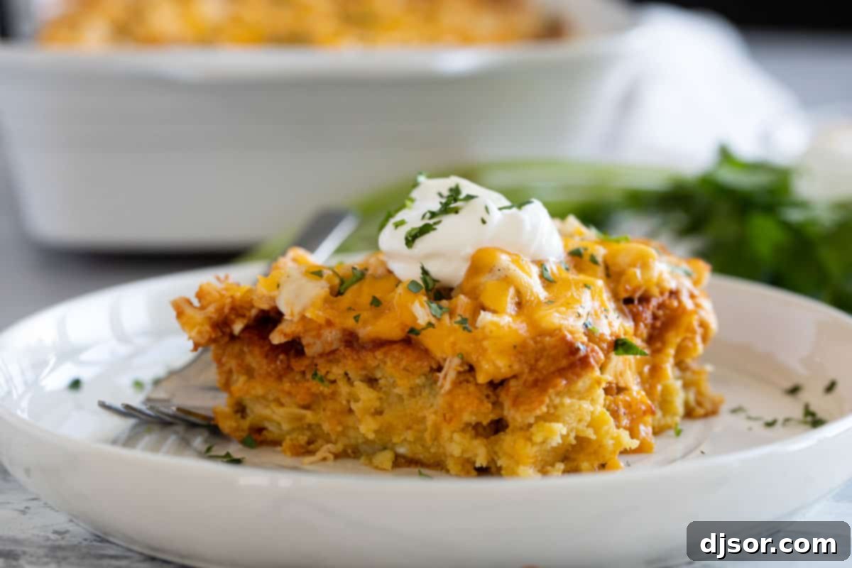 A delicious Chicken Tamale Casserole slice, generously topped with a dollop of sour cream and fresh cilantro, served on a white plate.
