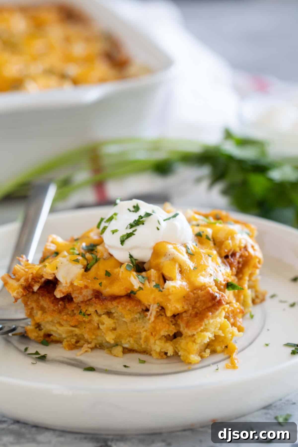 A perfect slice of Chicken Tamale Casserole, showing the layered corn crust, chicken, and melted cheese, garnished with sour cream and cilantro.