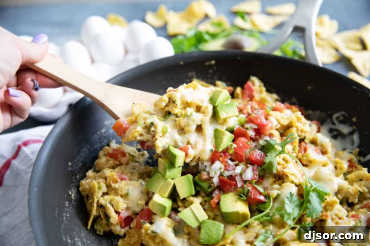 A close-up shot of Migas being scooped from a large nonstick skillet, showcasing the scrambled eggs, colorful vegetables, and crispy tortilla pieces.