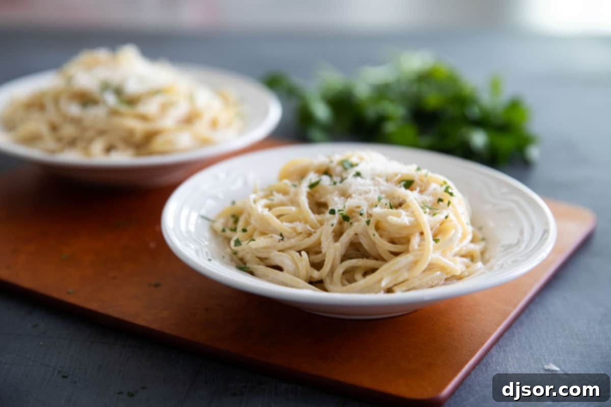 Two bowls of creamy Parmesan pasta, garnished with fresh parsley and extra grated cheese, ready to serve.