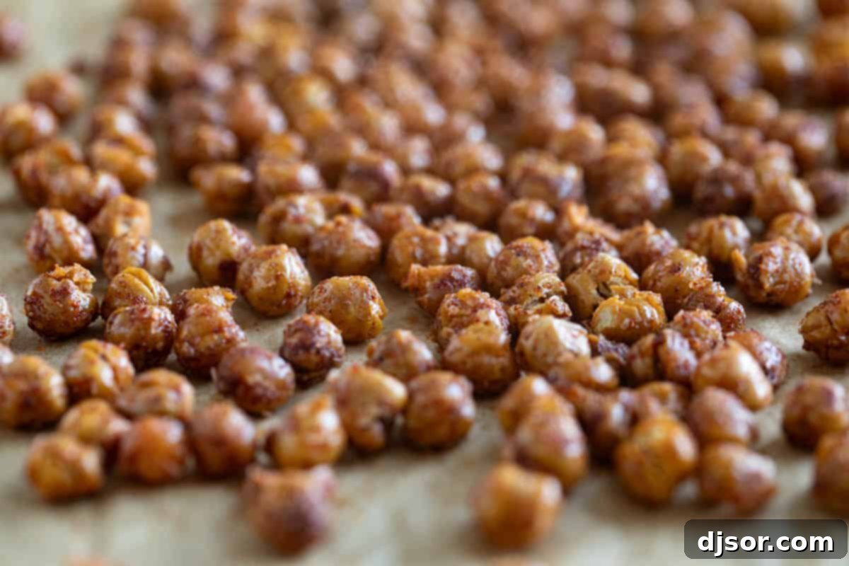 Crispy roasted chickpeas seasoned with spices, spread out in a single layer on parchment paper on a baking sheet.