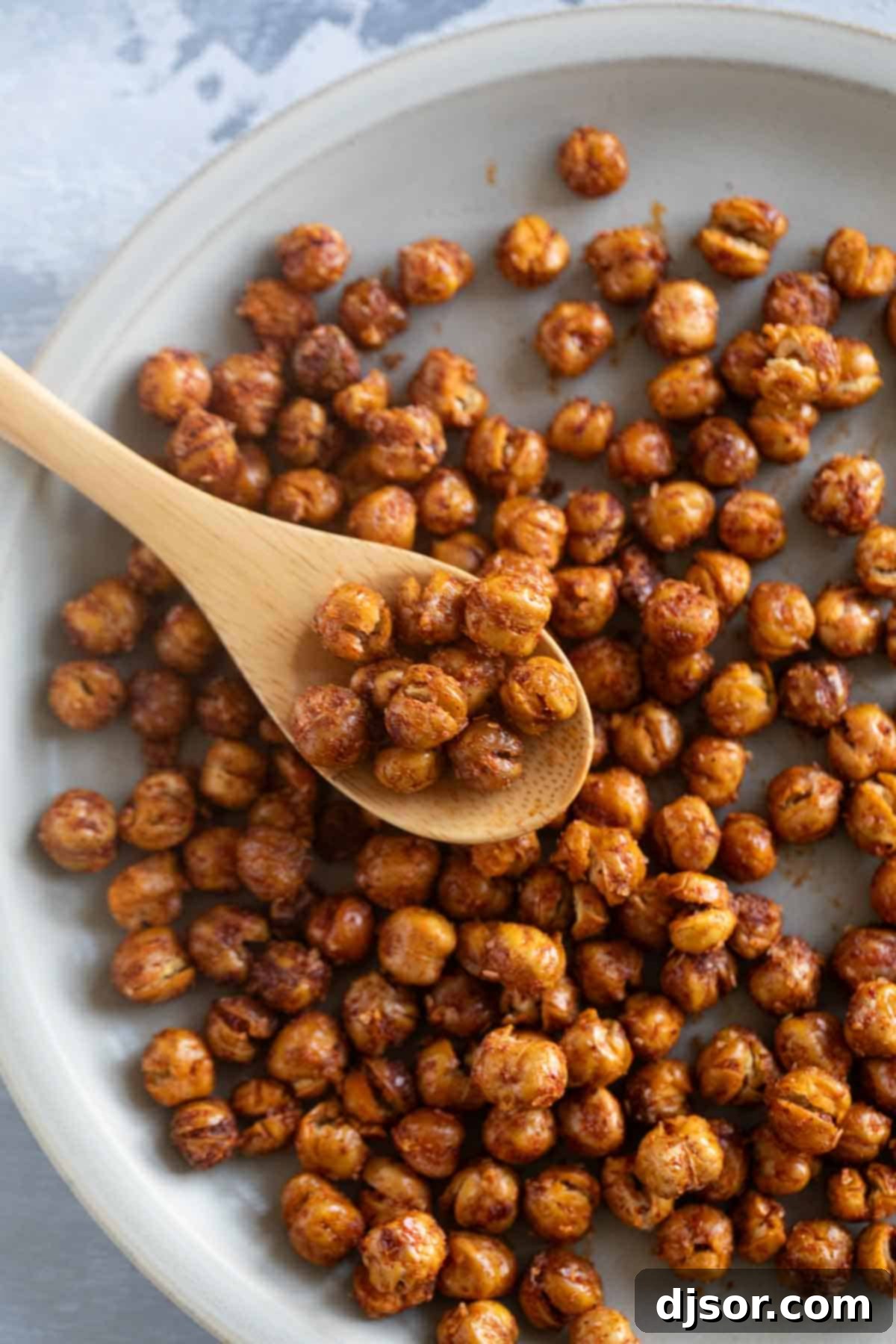 A small white plate filled with crispy, spiced roasted chickpeas, with a wooden spoon resting beside it, ready for a healthy snack.