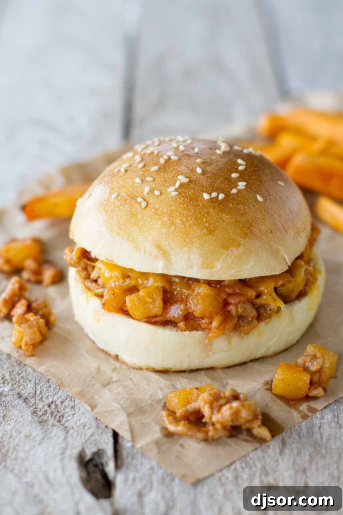 Hawaiian sloppy joes with filling falling out of a bun, garnished with shredded cheese.