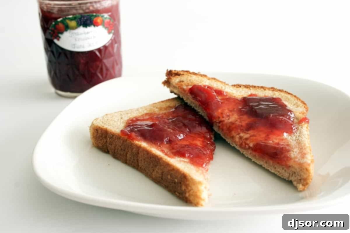 Toast topped with vibrant red homemade strawberry rhubarb jam, garnished with fresh mint, sitting on a rustic wooden table.