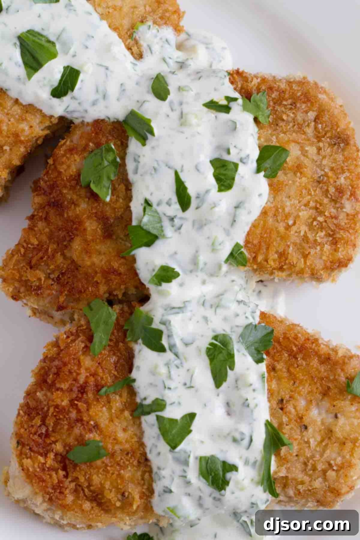 Crispy Panko Pork Chops with Creamy Herb Sauce 2 Juicy panko pork chops on a plate, generously topped with fresh, creamy herb dressing.