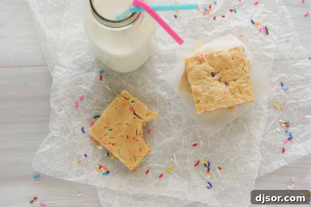 Close-up shot of golden Cake Batter Blondies, generously studded with vibrant rainbow sprinkles and melted white chocolate, showcasing their perfectly chewy texture and festive appeal.