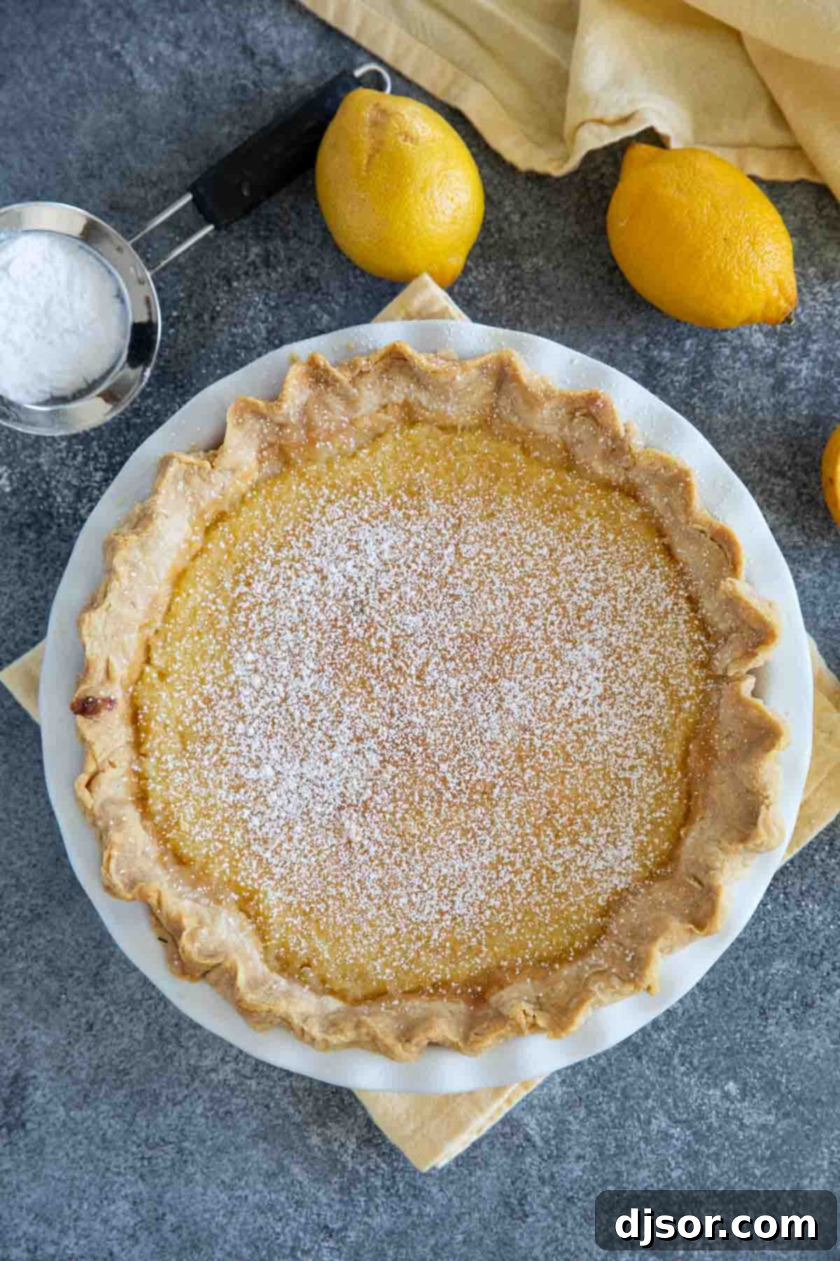 A freshly baked Lemon Chess Pie, dusted with powdered sugar, sits on a white cooling rack.