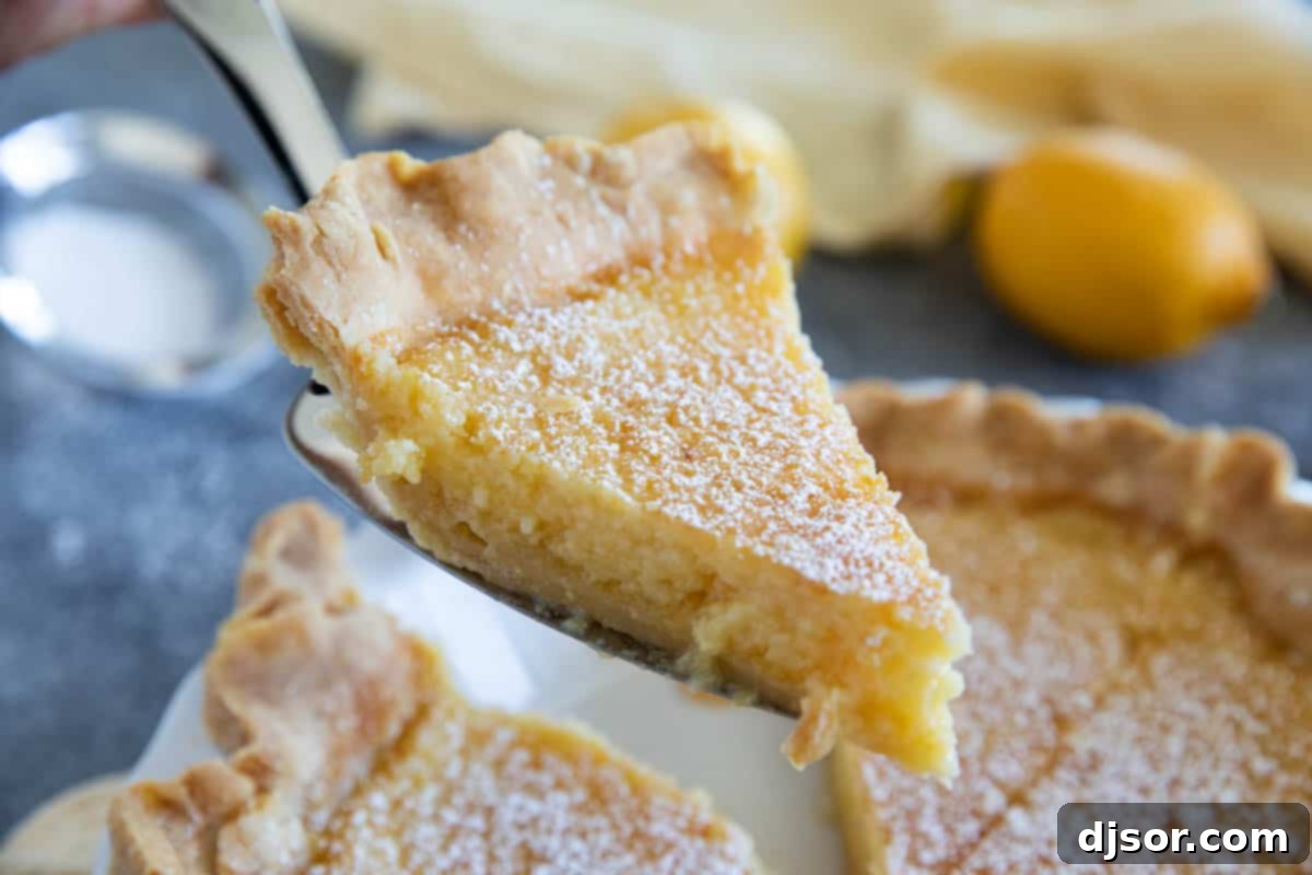 A hand gently removes a perfect slice of Lemon Chess Pie from a full pie, revealing its creamy, yellow filling and flaky crust.