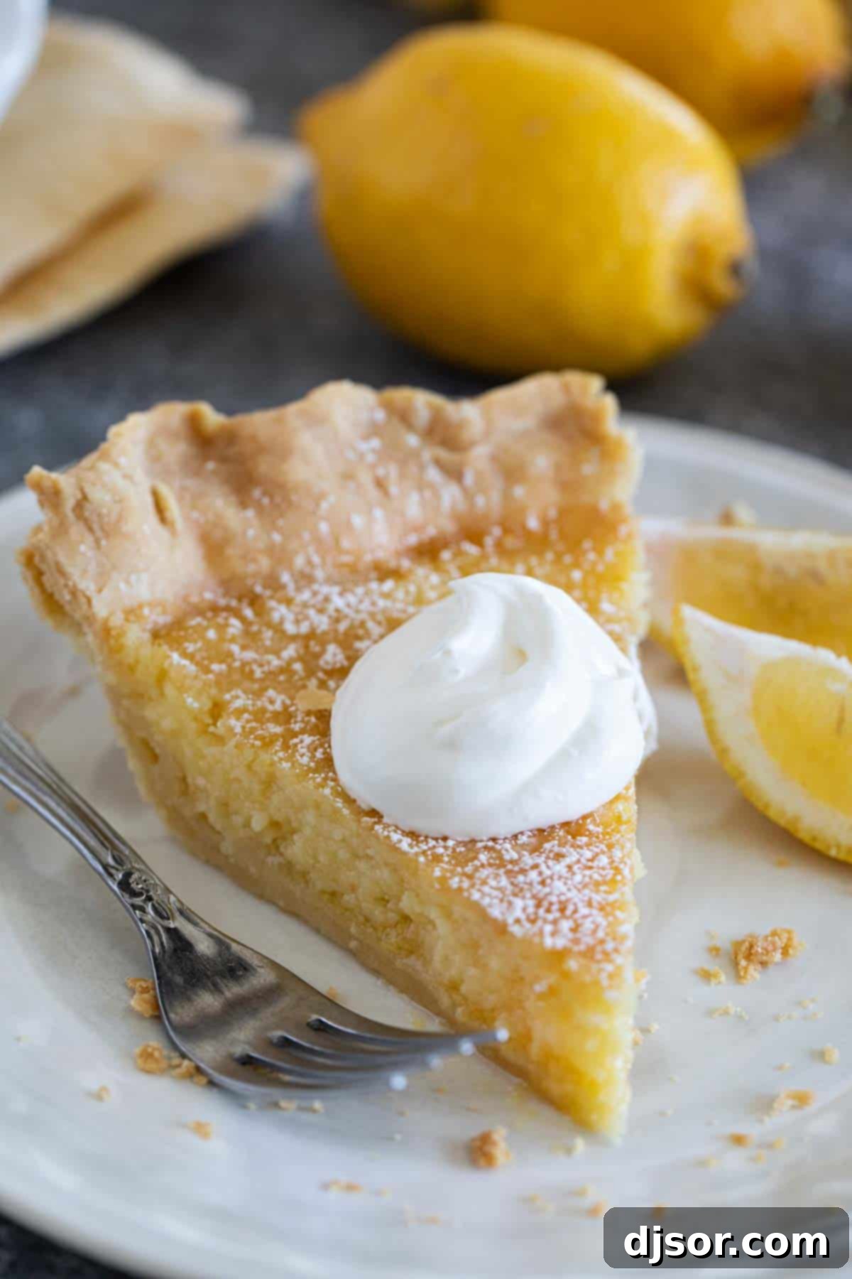 A delicious slice of Lemon Chess Pie, beautifully plated and topped with a generous swirl of fresh whipped cream and a sprinkle of lemon zest.