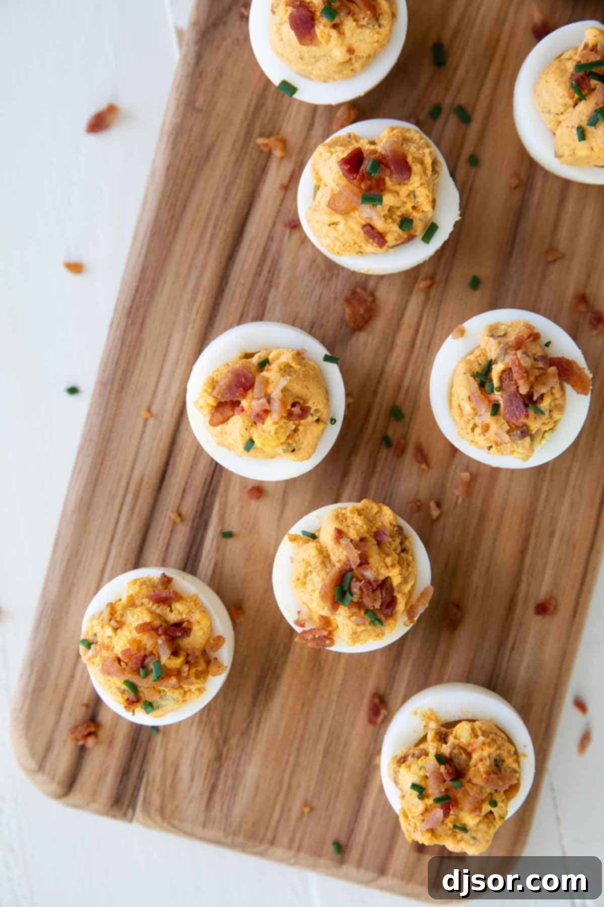 Savory Delights: Deviled Eggs with Crispy Bacon Perfectly arranged Deviled Eggs with Bacon on a dark cutting board, garnished with fresh chives, ready for serving. The presentation emphasizes the dish's freshness and visual appeal.