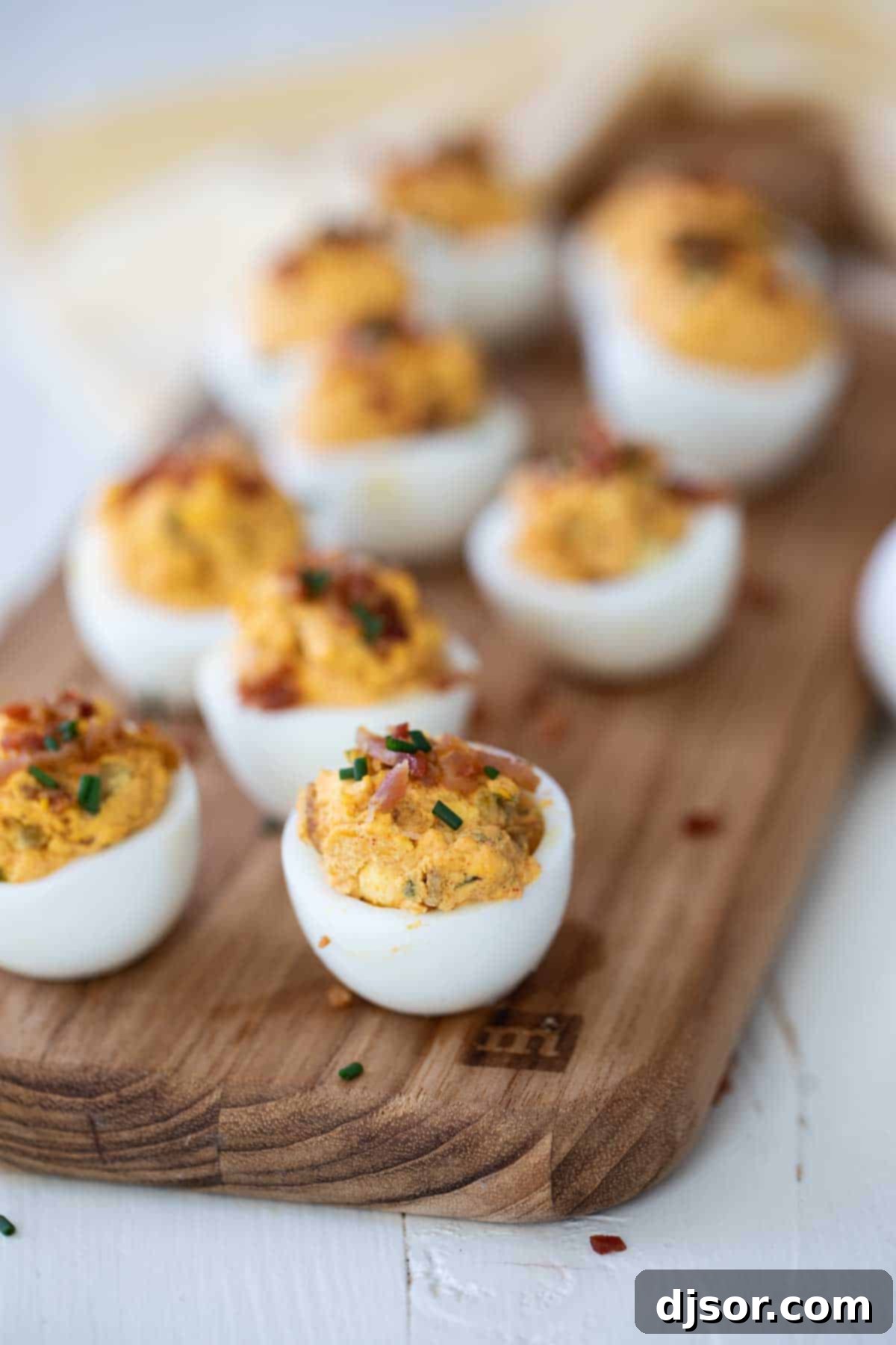 Creamy, Savory, and Irresistible: Easy Deviled Eggs with Bacon A vibrant close-up of an Easy Deviled Egg with Bacon, featuring its perfectly piped, creamy filling, generously sprinkled with crispy bacon bits and fresh chives, ready to be enjoyed.