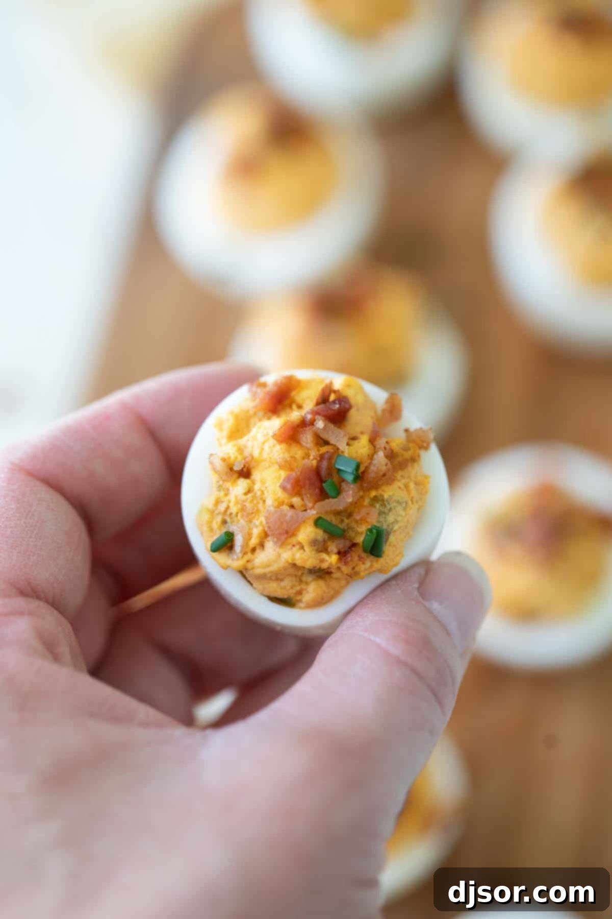 Irresistible Deviled Eggs with Bacon: A Must-Try Appetizer A hand gently reaching for a delicious deviled egg with bacon, highlighting its enticing nature and readiness to be savored, perfect for any casual or festive setting.