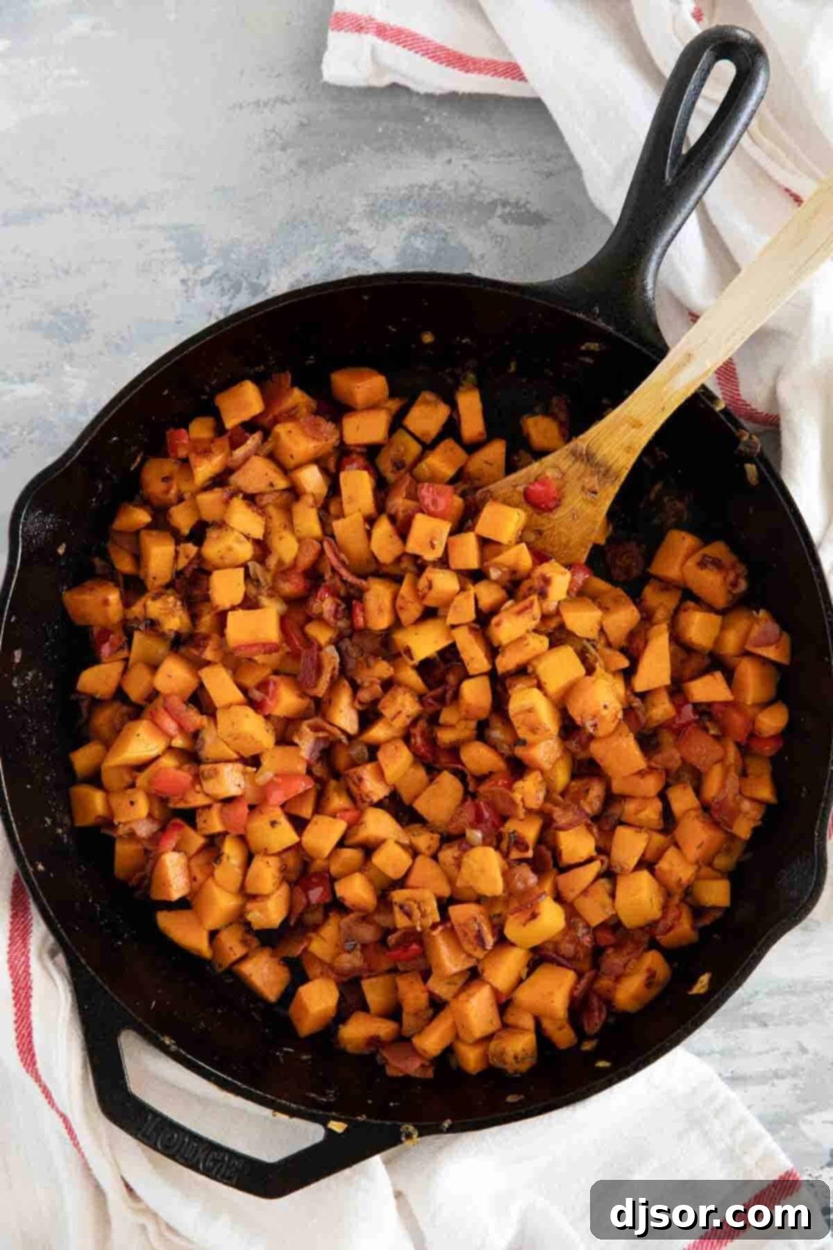 The perfect Sweet Potato Hash – sweet potatoes are combined with bacon, onions and sweet red peppers in this easy stovetop dish. Serve it as a side dish or add an egg on top and turn it into breakfast. Close-up of a cast iron skillet filled with colorful Sweet Potato Hash, garnished with fresh herbs, ready to be served.