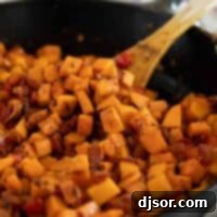 Golden Sweet Potato Hash 2 A wooden spoon resting in a skillet full of Sweet Potato Hash, highlighting the rustic appeal of the dish.
