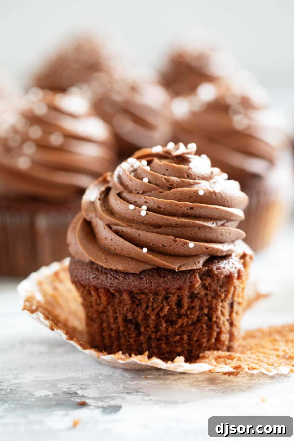 Decadent Eggless Chocolate Cupcakes with smooth chocolate frosting, one wrapper peeled back to show the moist cake inside.