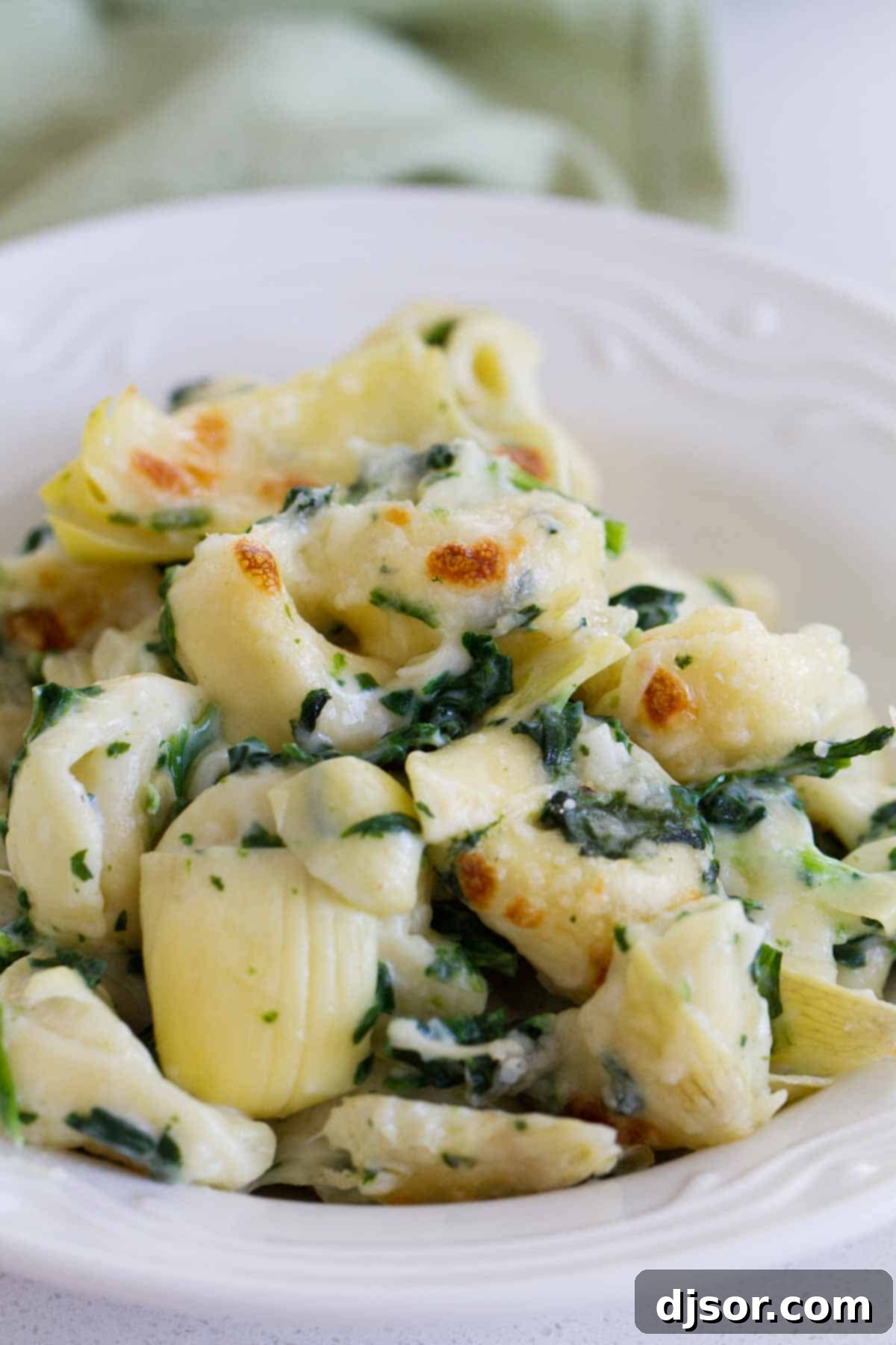 A single serving of creamy Spinach and Artichoke Tortellini Bake in a shallow white bowl, highlighting the texture of the tortellini and sauce.
