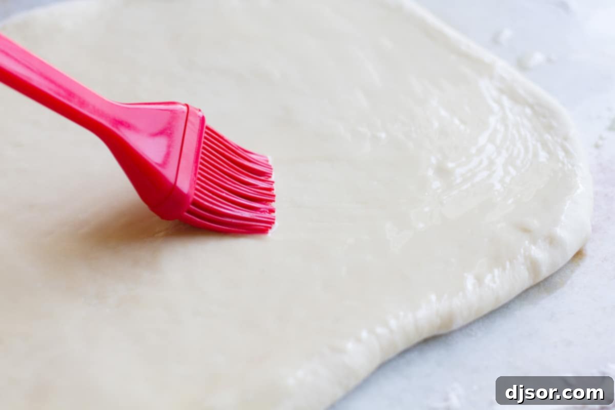 Melted butter being brushed onto the surface of the dough rectangle.