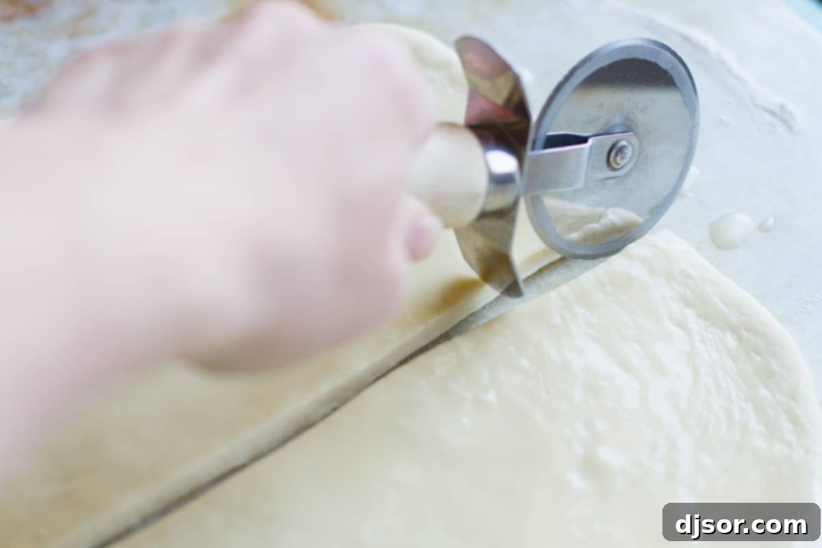 Cutting the Dough Horizontally A pizza cutter slicing the buttered dough horizontally down the middle of the 14-inch side, creating two long strips.