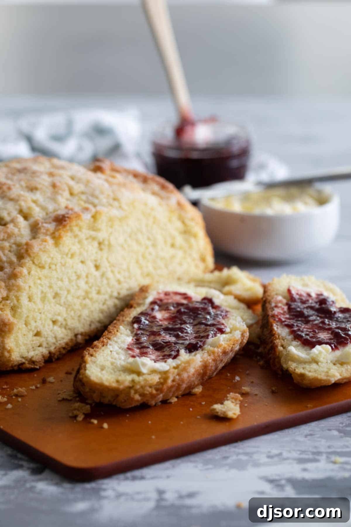 A golden-brown loaf of Irish Soda Bread, sliced and ready to serve with a side of rich, vibrant jam.
