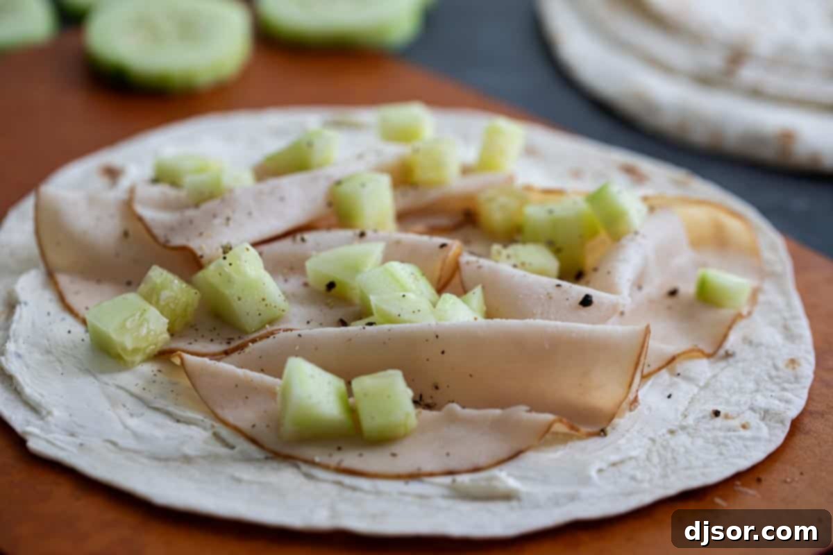 A close-up view of the fresh and colorful ingredients that go into making a delicious Turkey Wrap, including deli turkey, sliced cucumbers, and a creamy spread.