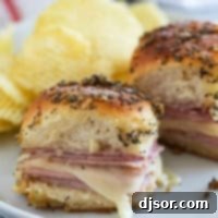 Two ham and cheese sliders on a plate with potato chips, ready to eat.