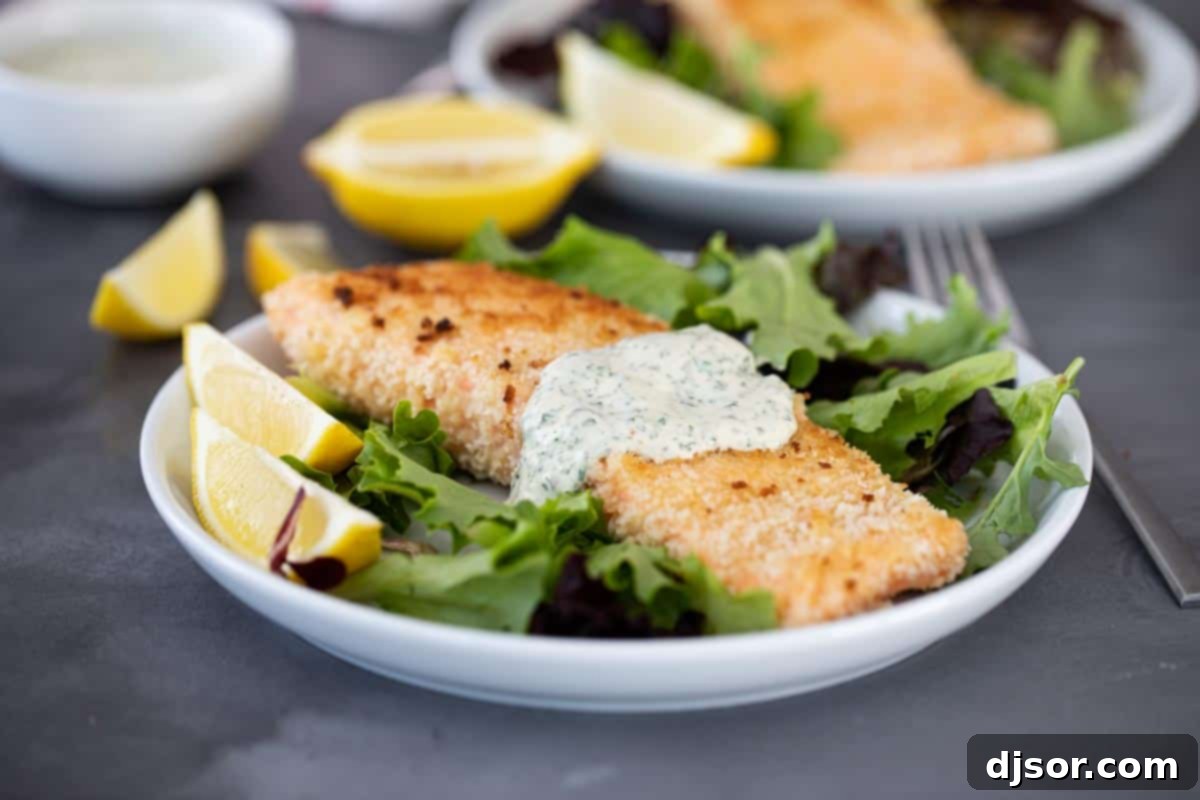 An easy weeknight dinner, this Pan Fried Salmon with Remoulade looks fancy but is super simple! Panko crusted salmon is cooked on the stovetop with a simple, flavorful sauce. Close-up of perfectly pan-fried salmon on a plate, garnished with fresh herbs and a dollop of creamy remoulade sauce.