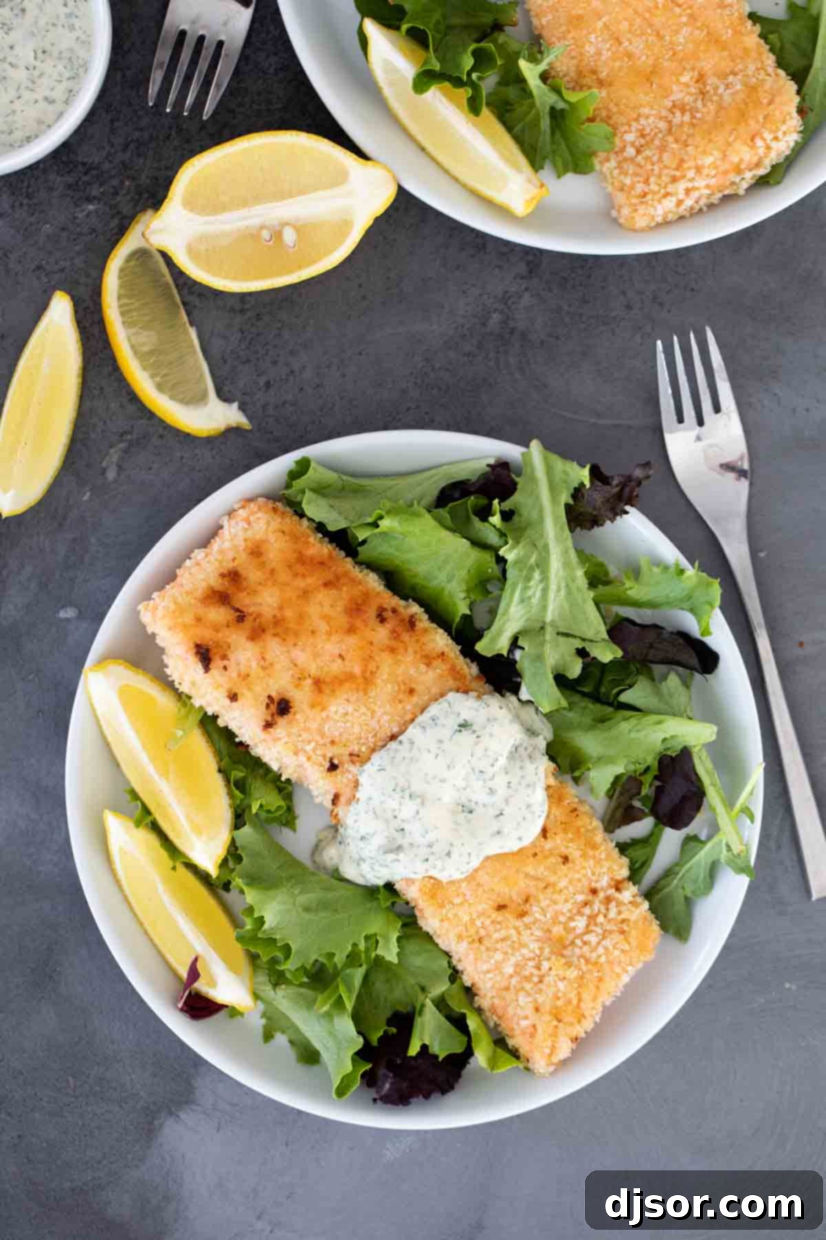An easy weeknight dinner, this Pan Fried Salmon with Remoulade looks fancy but is super simple! Panko crusted salmon is cooked on the stovetop with a simple, flavorful sauce. A close-up view of a plate featuring pan-fried salmon with a generous serving of remoulade sauce, ready to be enjoyed.