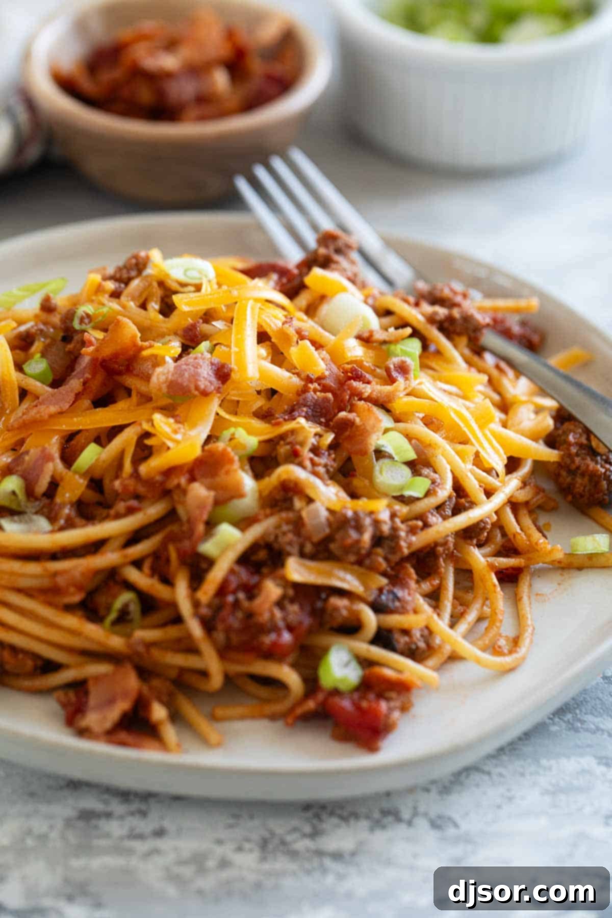 Plate of Cowboy Spaghetti with ground beef, bacon, cheese, and green onions.