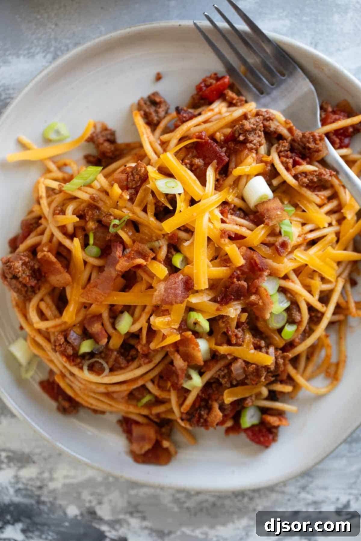 Plate full of Cowboy Spaghetti topped with shredded cheddar cheese.