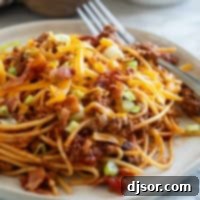 Plate of Cowboy Spaghetti with ground beef, bacon, cheese, and green onions.