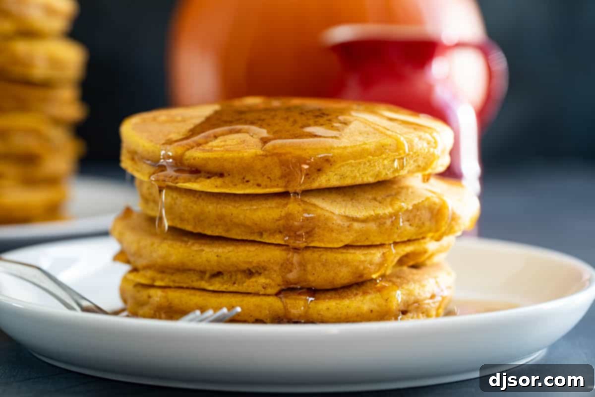 Stack of fluffy pumpkin pancakes topped with syrup and a dusting of powdered sugar, ready for a delicious fall breakfast.