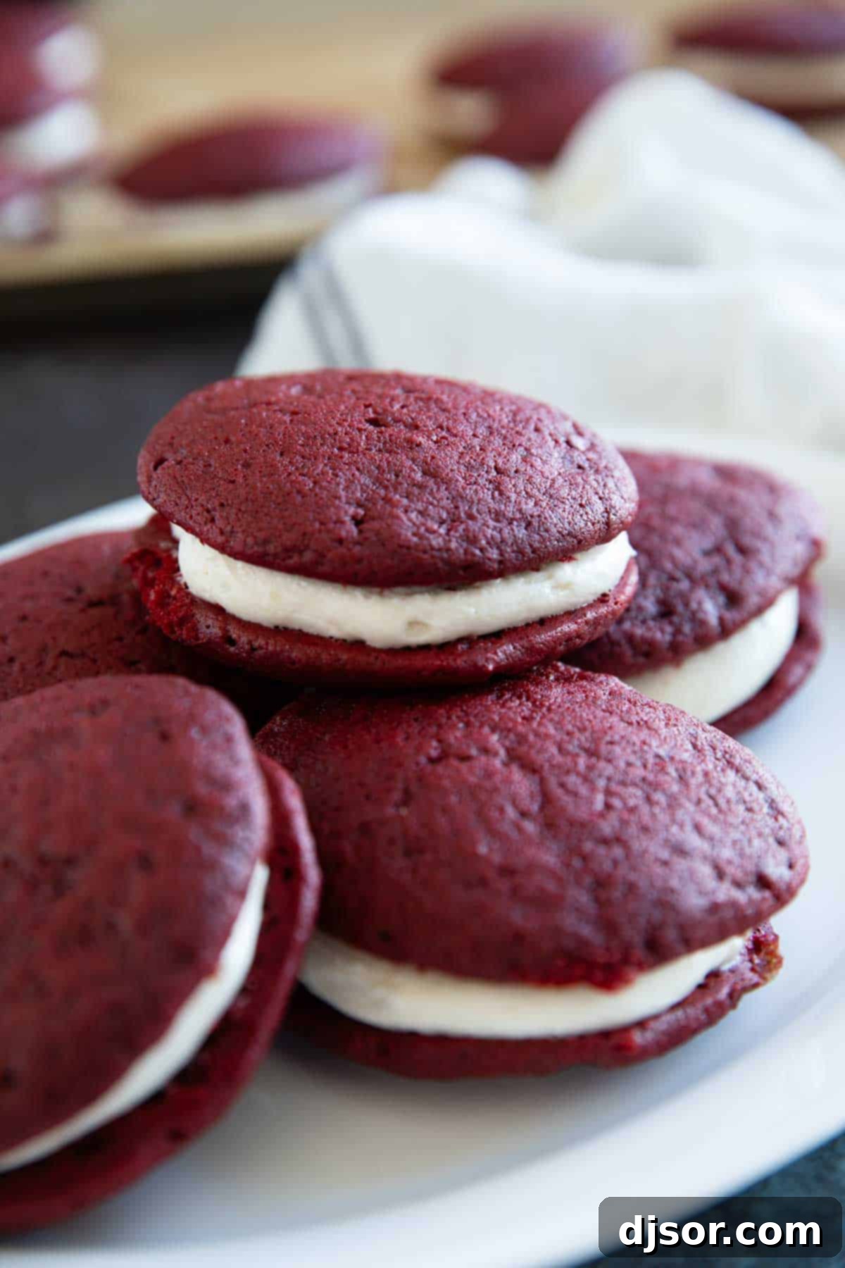 A stack of beautifully assembled Red Velvet Whoopie Pies on a white plate, showcasing their inviting texture and rich color, ready to be enjoyed.
