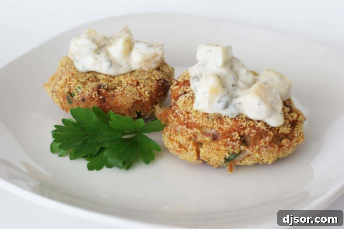 Golden-brown salmon and corn cakes generously topped with a creamy, colorful mango tartar sauce, served on a plate as a delicious meal.