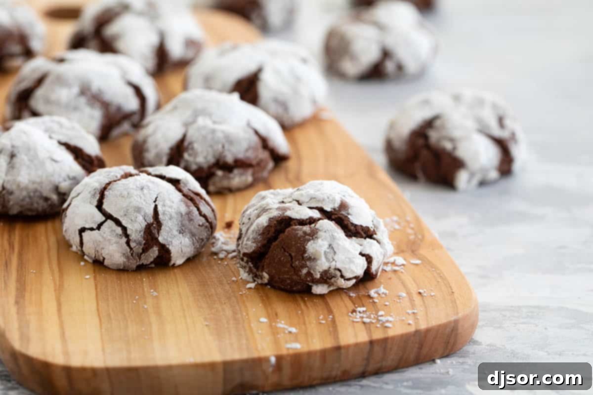 Puffy chocolate crinkle cookies with a dusting of white powdered sugar, arranged on a rustic cutting board, showcasing their inviting crinkled texture.