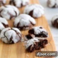 A cutting board displaying an assortment of chocolate crinkle cookies, with one cookie broken to show its soft, fudgy interior.