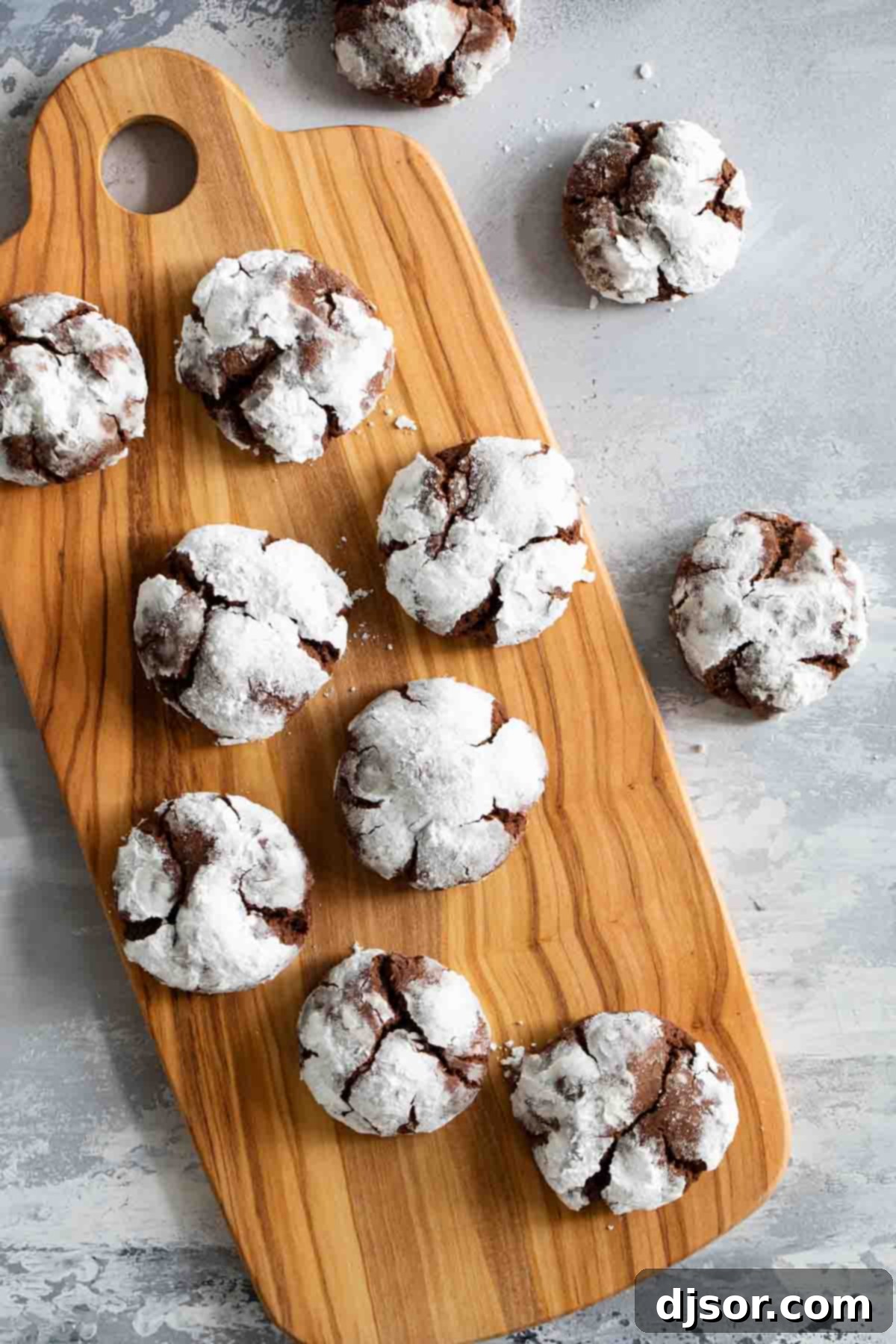 Close-up shot of several chocolate crinkle cookies generously dusted in powdered sugar, resting on a wooden board, highlighting their beautiful cracked surface.